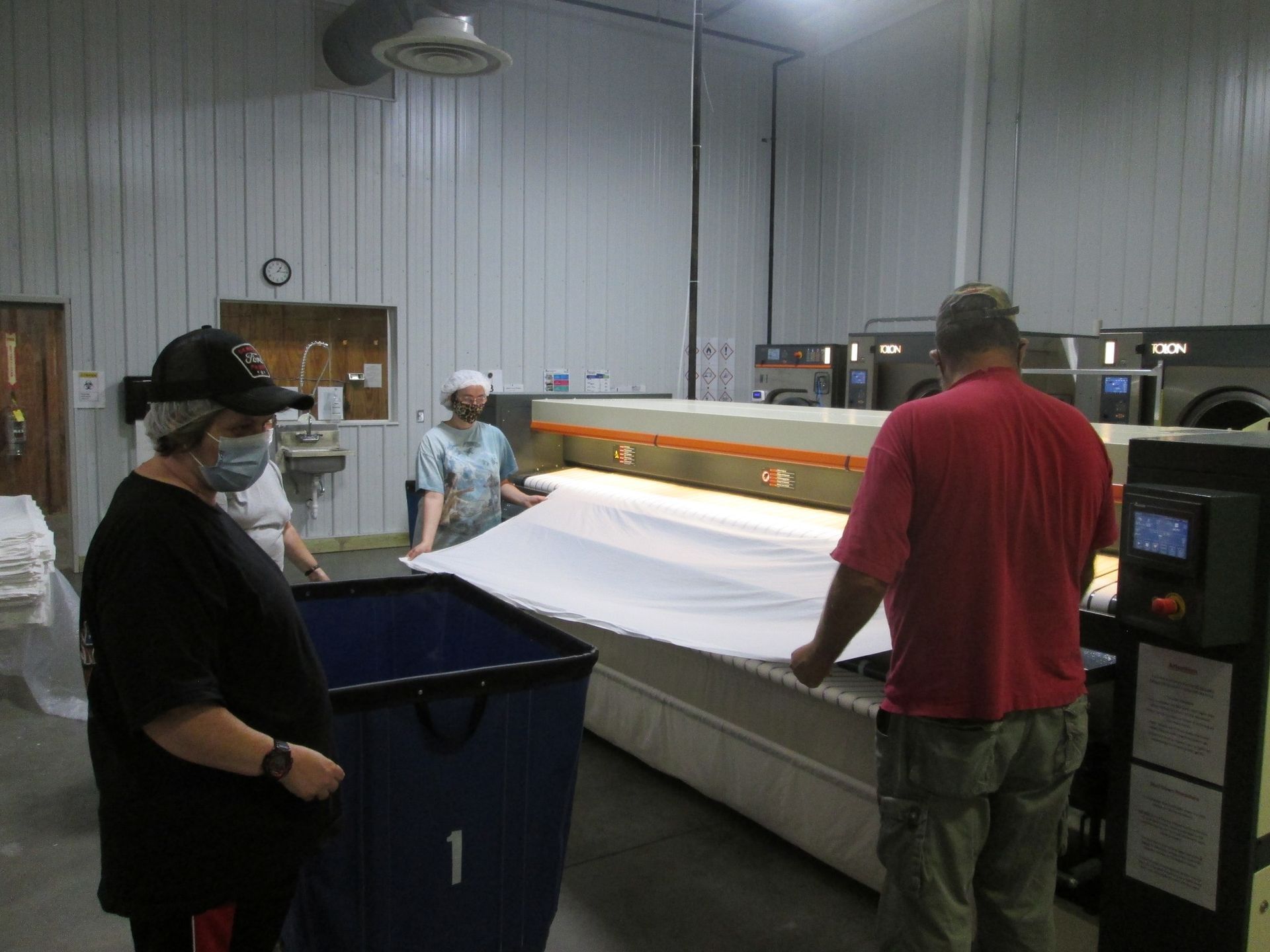 People folding a large white sheet in a laundry facility.