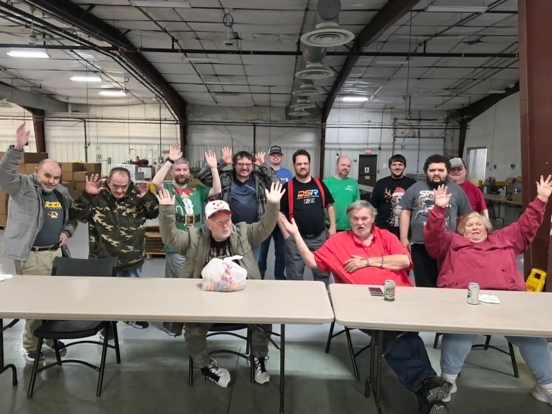 Group of people inside a building, arms raised with smiles. They sit at tables.