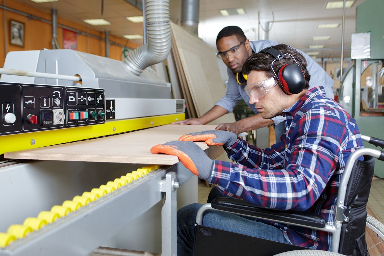 Person in wheelchair using woodworking machine with assistance from a supervisor. Person in wheelchair using woodworking machine with assistance from a supervisor.