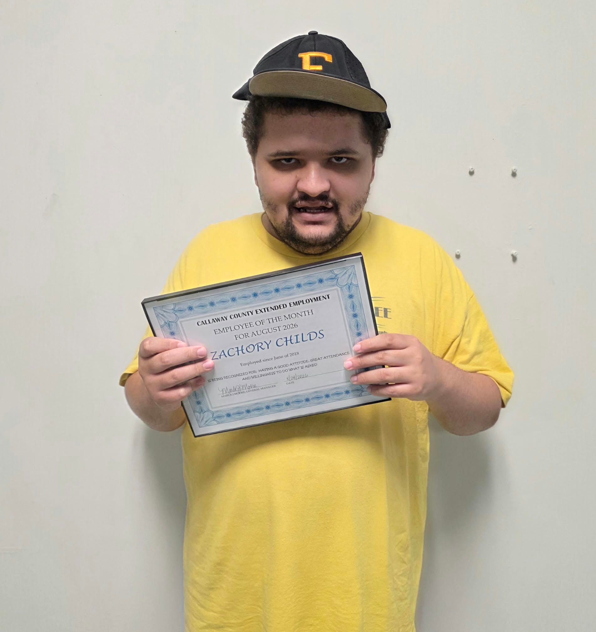 Person in a yellow shirt holding a certificate against a plain wall. Person in a yellow shirt holding a certificate against a plain wall.
