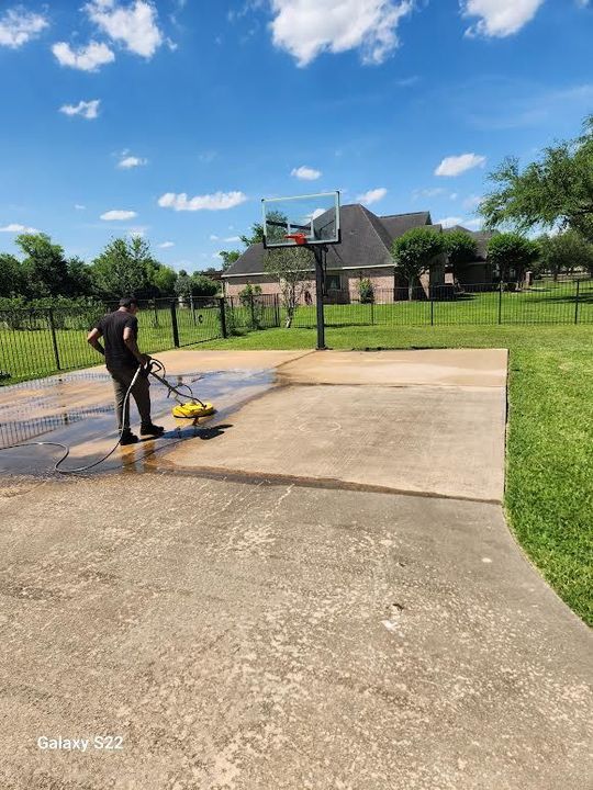 A close-up shot of a metal garden hose nozzle spraying a fan of water onto a concrete surface.