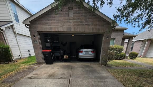 Front view of a brick two-car garage with one car parked inside and a driveway in front.