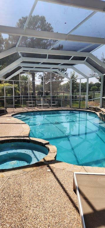 Screened-in pool and spa with turquoise water and lounge chairs in a sunny backyard