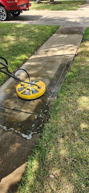 A person wearing blue overalls uses a pressure washer to clean the light-colored siding of a house.