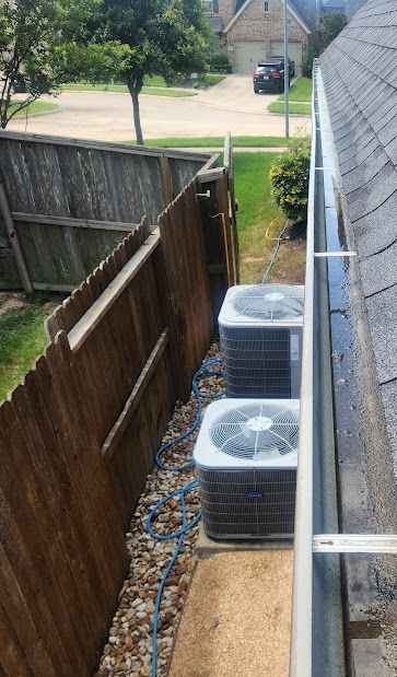 Narrow side yard with two outdoor AC units beside a house and wooden fence, overlooking a street.