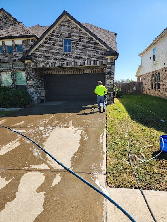 Person pressure washing a wet driveway in front of a stone house with a garage.