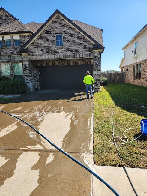 Person pressure washing a wet driveway in front of a stone house with a garage.