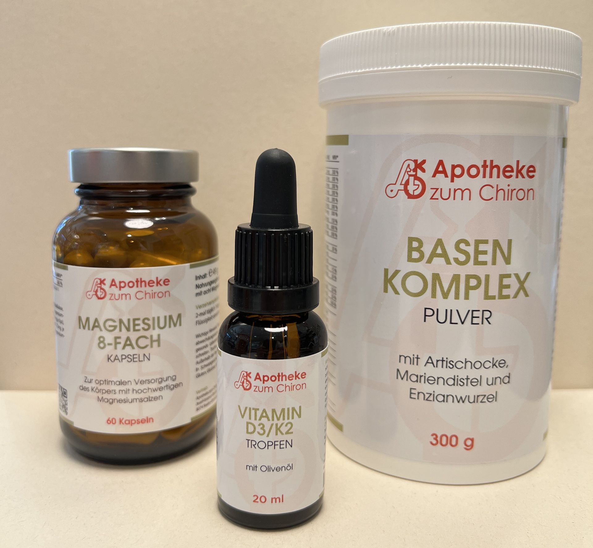Drei Apotheke zum Chiron-Nahrungsergänzungsmittelbehälter: Magnesiumkapseln, Vitamin D3/K2-Tropfen und Basiskomplexpulver.
