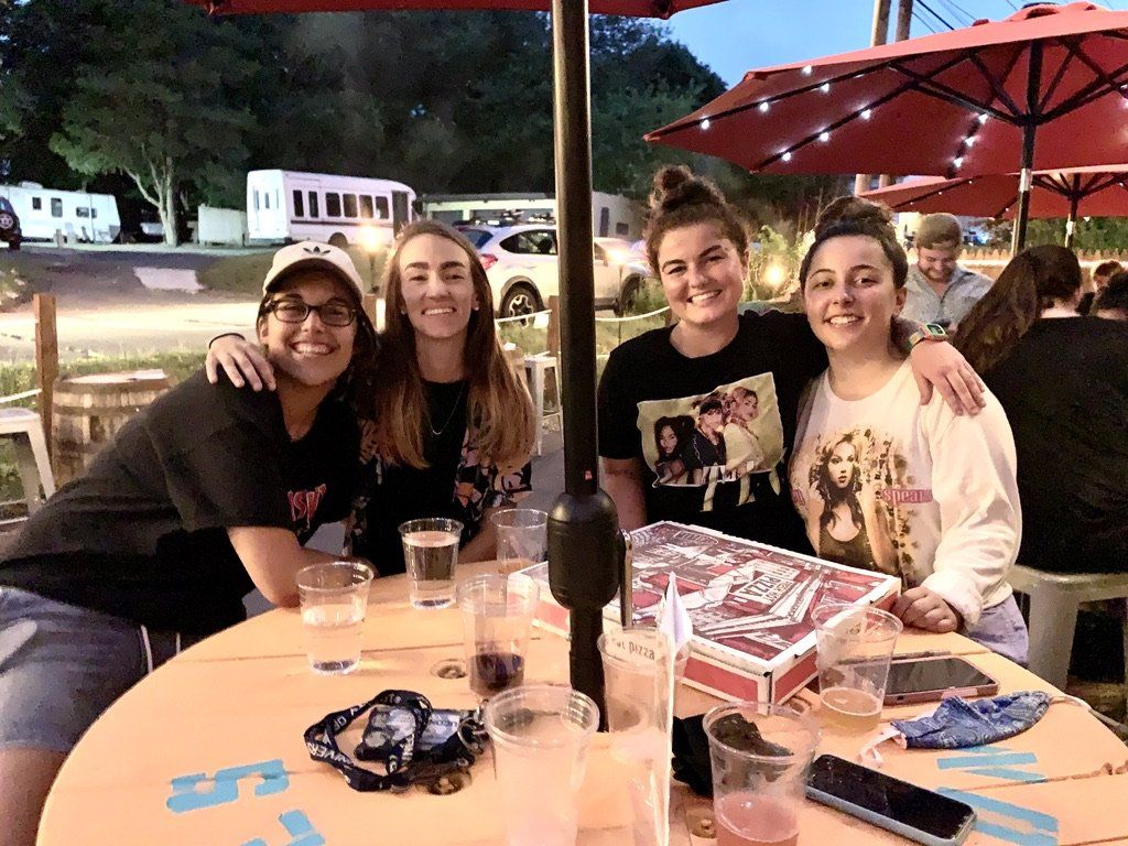 Four people smiling, posing around a table, outdoors, under umbrellas.