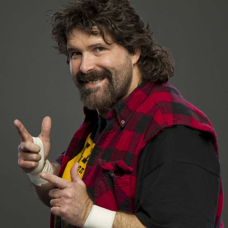 Wrestler with a beard, wearing a plaid vest, flashing a 