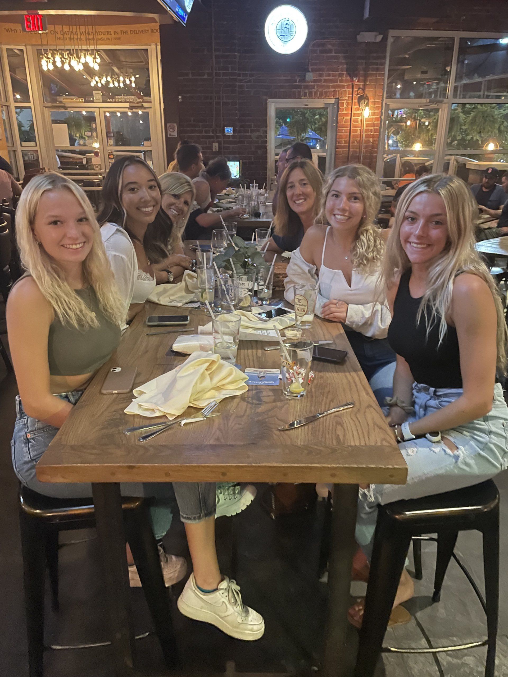 A group of six women smiles while seated at a table in a restaurant.