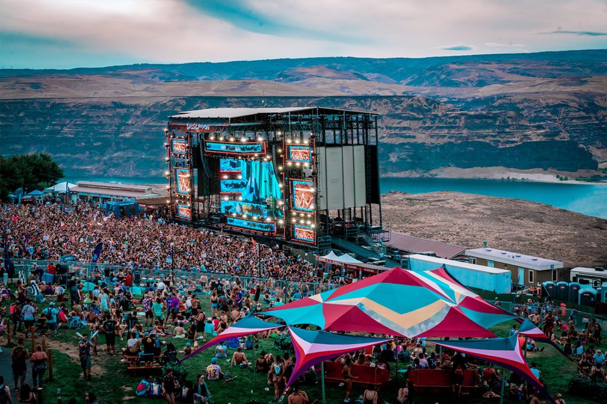 A large crowd of people are sitting in front of a stage at a music festival.