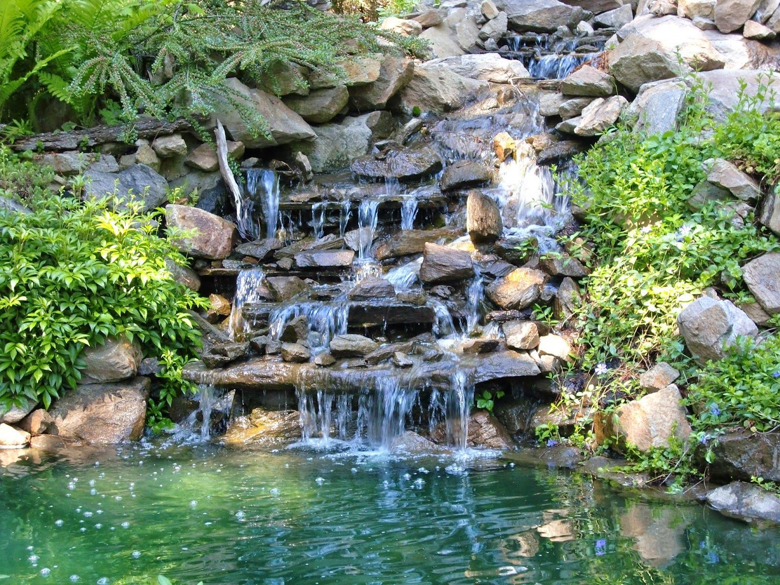 There is a waterfall in the middle of a pond surrounded by rocks.