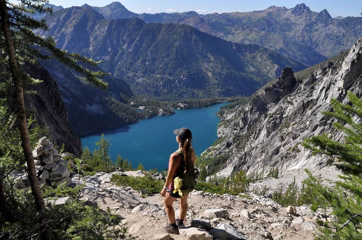 A woman is standing on top of a mountain overlooking a lake.