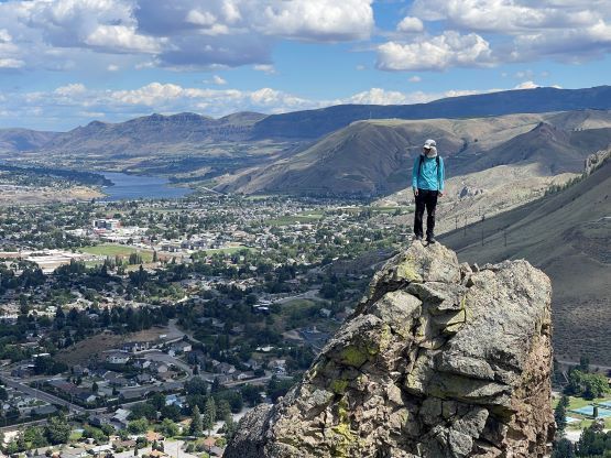 A woman is standing on top of a rocky mountain overlooking a city.