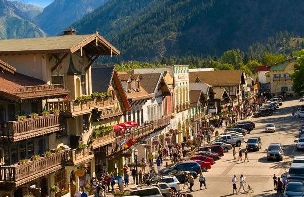 A group of people are walking down a street in a small town with mountains in the background.