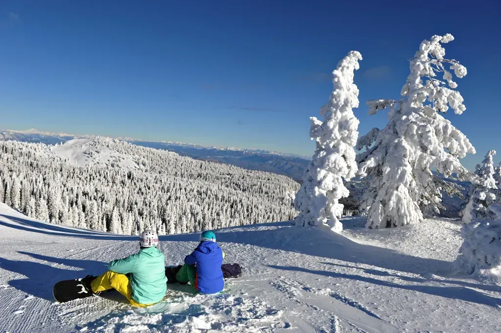 Two snowboarders are sitting on top of a snow covered mountain.