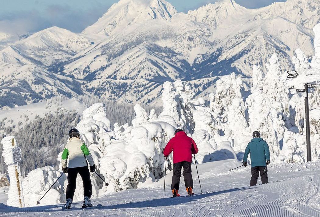 Three people skiing down a snow covered slope with mountains in the background