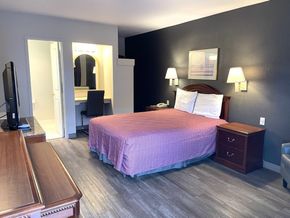 A hotel room with a king size bed , nightstand , dresser and television.
