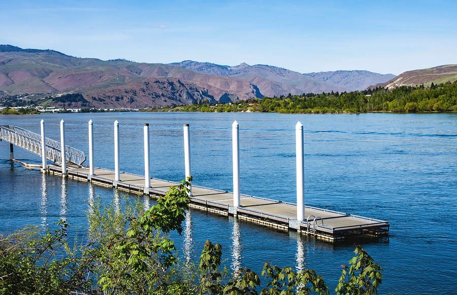 There is a dock in the middle of a lake with mountains in the background.