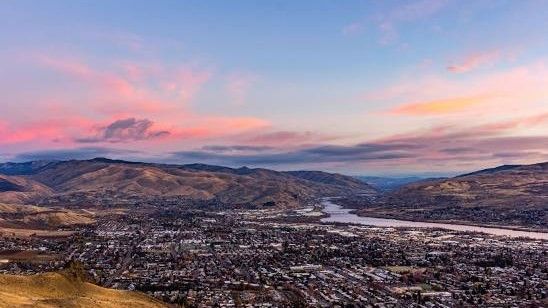 An aerial view of a city surrounded by mountains and a river at sunset.