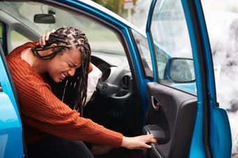 a woman is sitting in front of a damaged car.