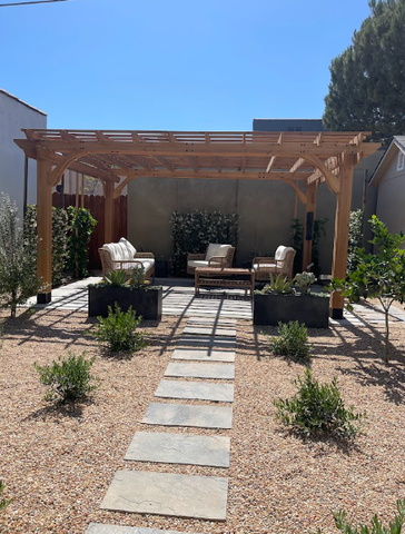 Modern backyard patio with wooden pergola, seating, stone path, and desert landscaping under a clear blue sky