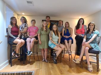 Group seated on tall stools in a bright room, posing for a photo.