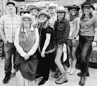 Group in cowboy hats posing in a rustic store aisle, with shelves and wooden decor in the background.