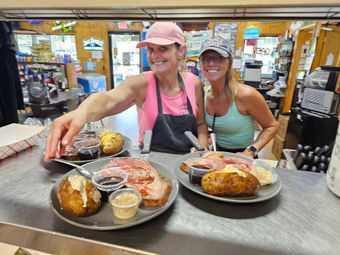 Two people smiling at a restaurant table with plates of pastries and coffee of counter-service.
