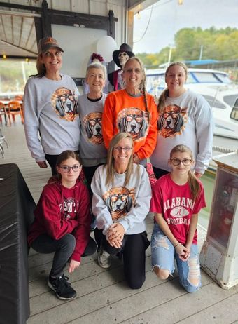 Seven people posing indoors in matching orange and gray shirts, smiling in front of a window.
