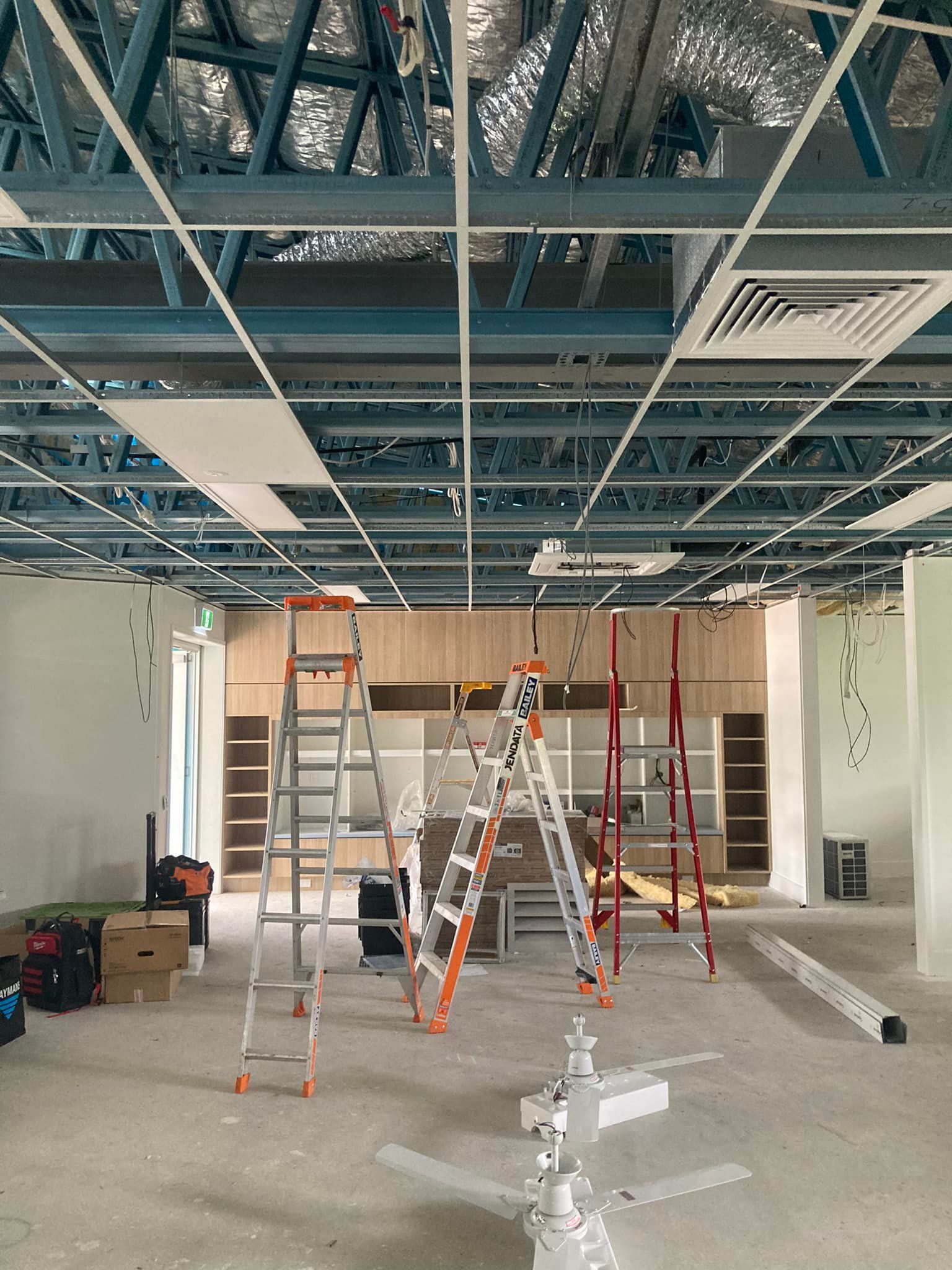 Interior construction site with ladders, unfinished ceiling grid, and partially built shelving — Jendata In Garbutt, QLD