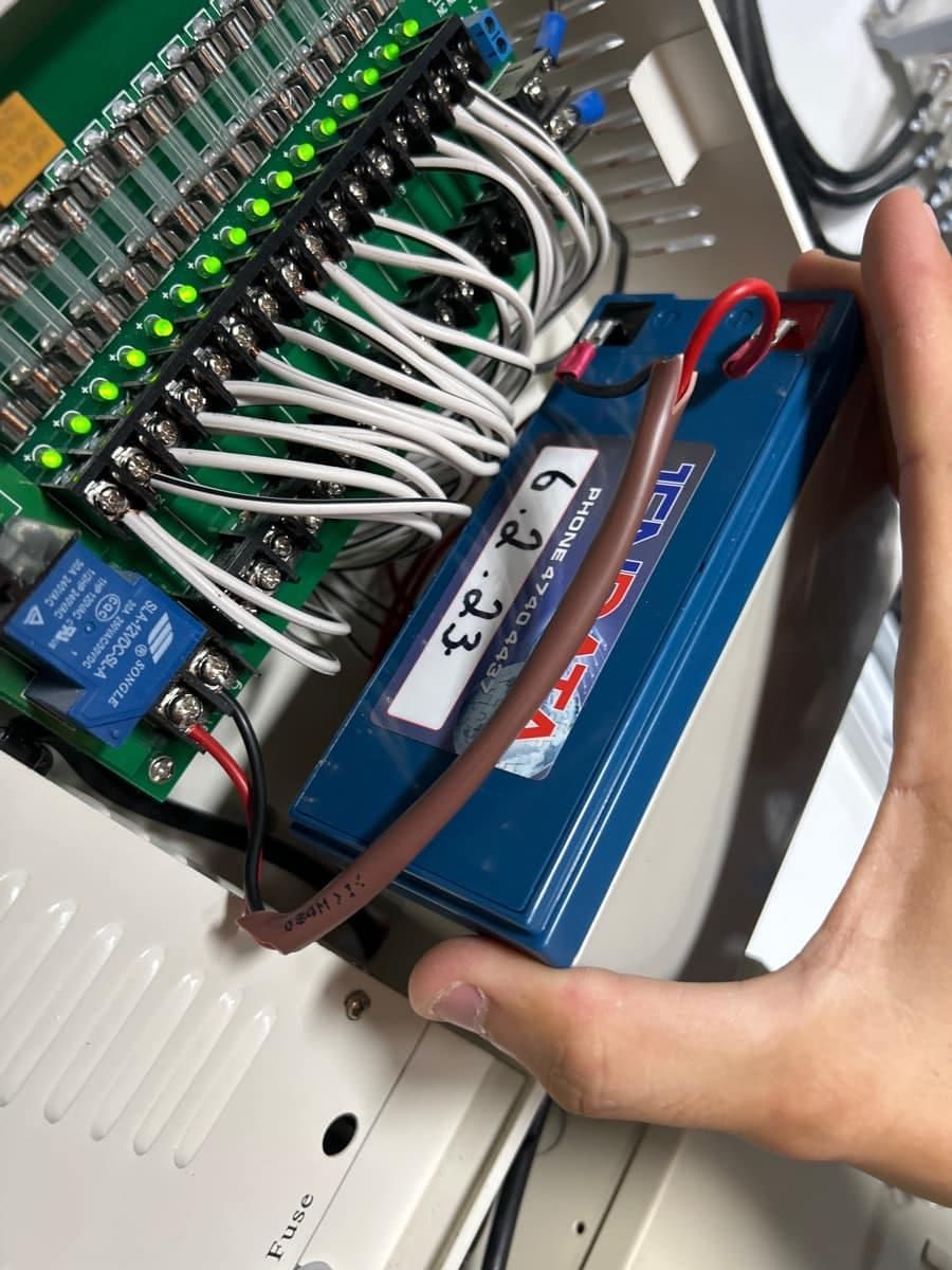 Hand Holding a Blue 12v Battery With Red and Black Wires Connected — Jendata In Ingham, QLD