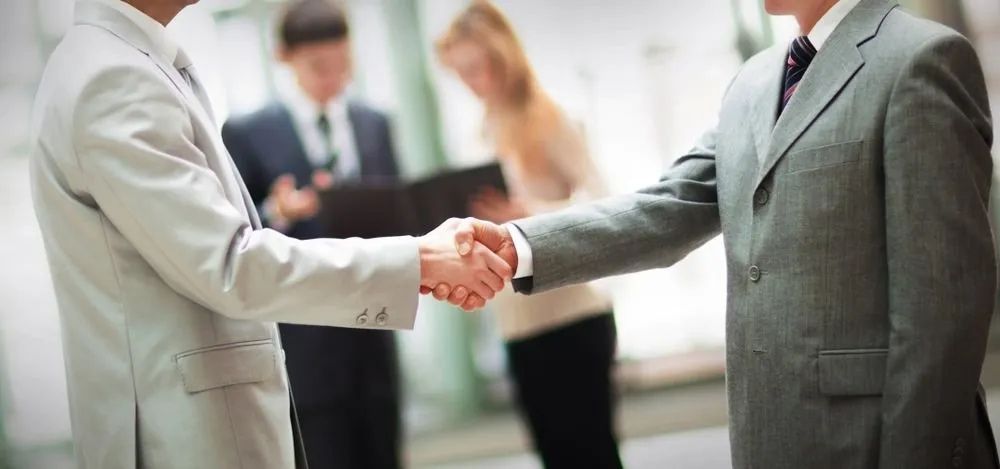 Two People in Suits Shaking Hands, Other People in the Blurred Background — Jendata In Garbutt, QLD