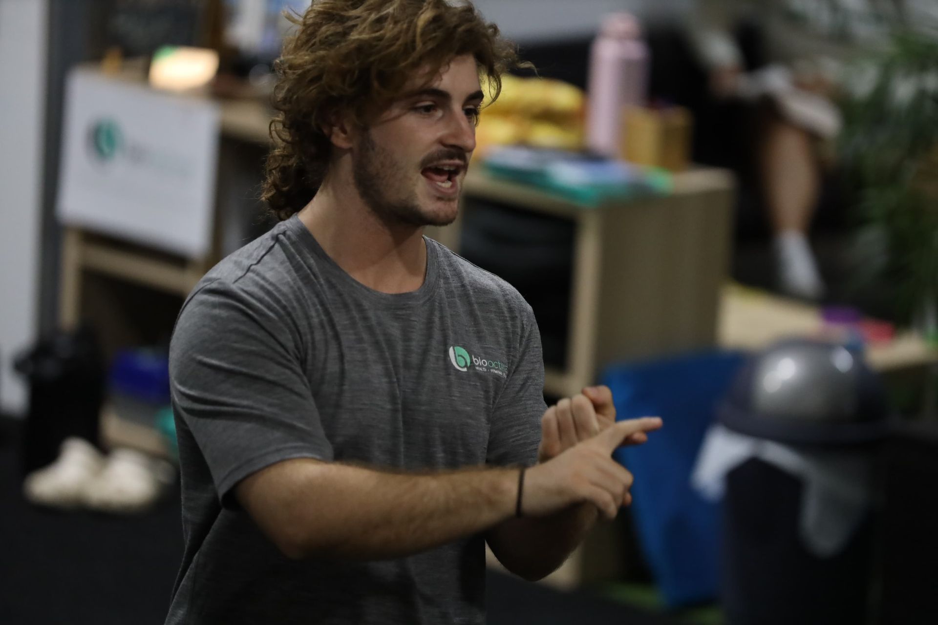 A man in a gray shirt is pointing at something in a room.