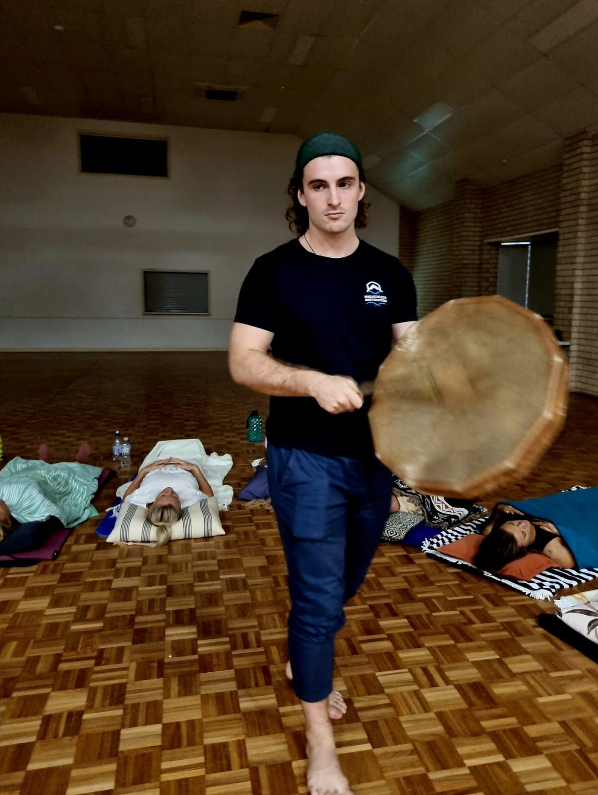 A man is standing on a wooden floor holding a drum.