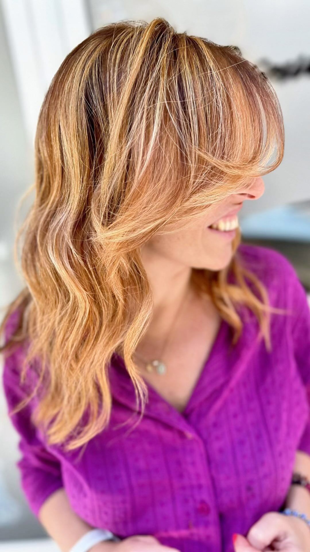 Una donna con i capelli biondi indossa una maglietta viola e sorride.