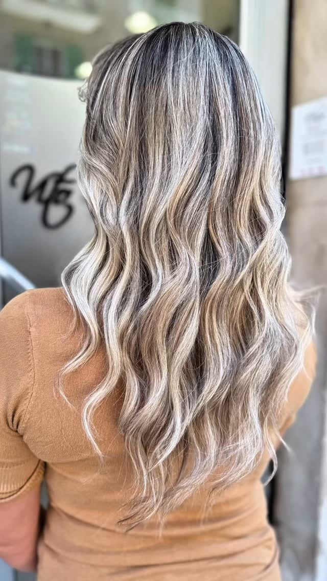 Una donna con lunghi capelli biondi e ondulati è in piedi davanti a una finestra.