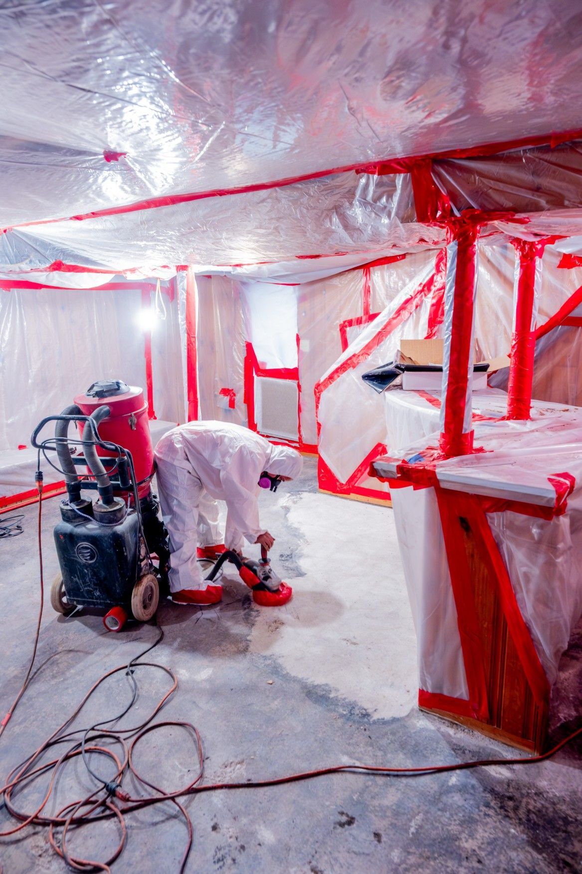 Red-taped construction area with equipment, tools, and plastic sheeting covering walls and ceiling.