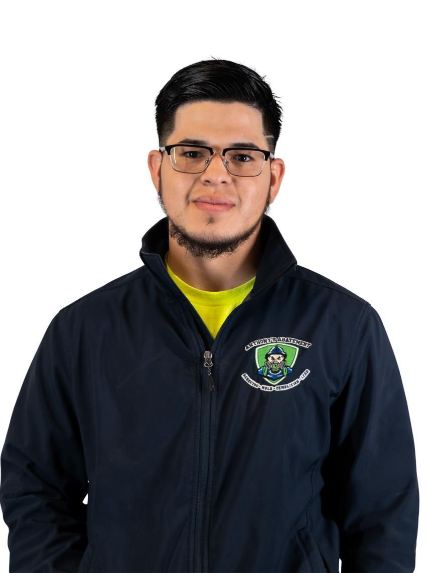 Person in a dark jacket with a logo, wearing glasses, standing against a white background
