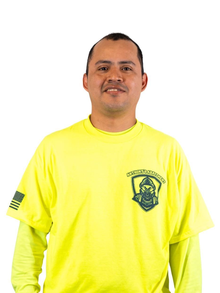 Man in a bright yellow T-shirt with a green emblem, standing against a white background.