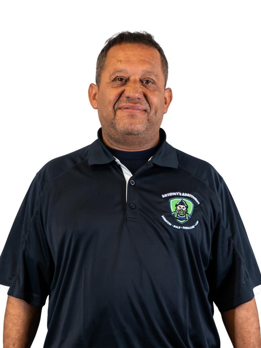 Man in a black polo shirt with a logo, standing against a white background.