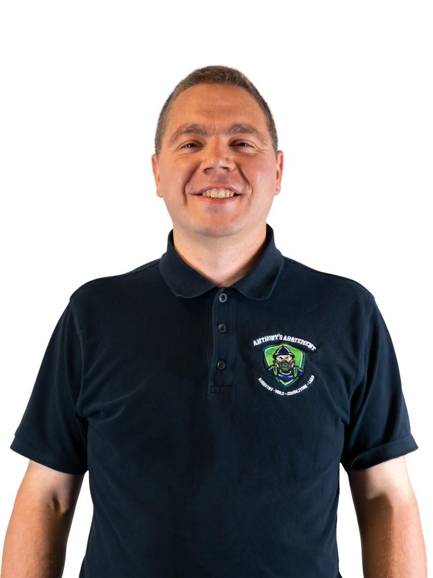 Man wearing a navy polo shirt with a logo, smiling against a white background.