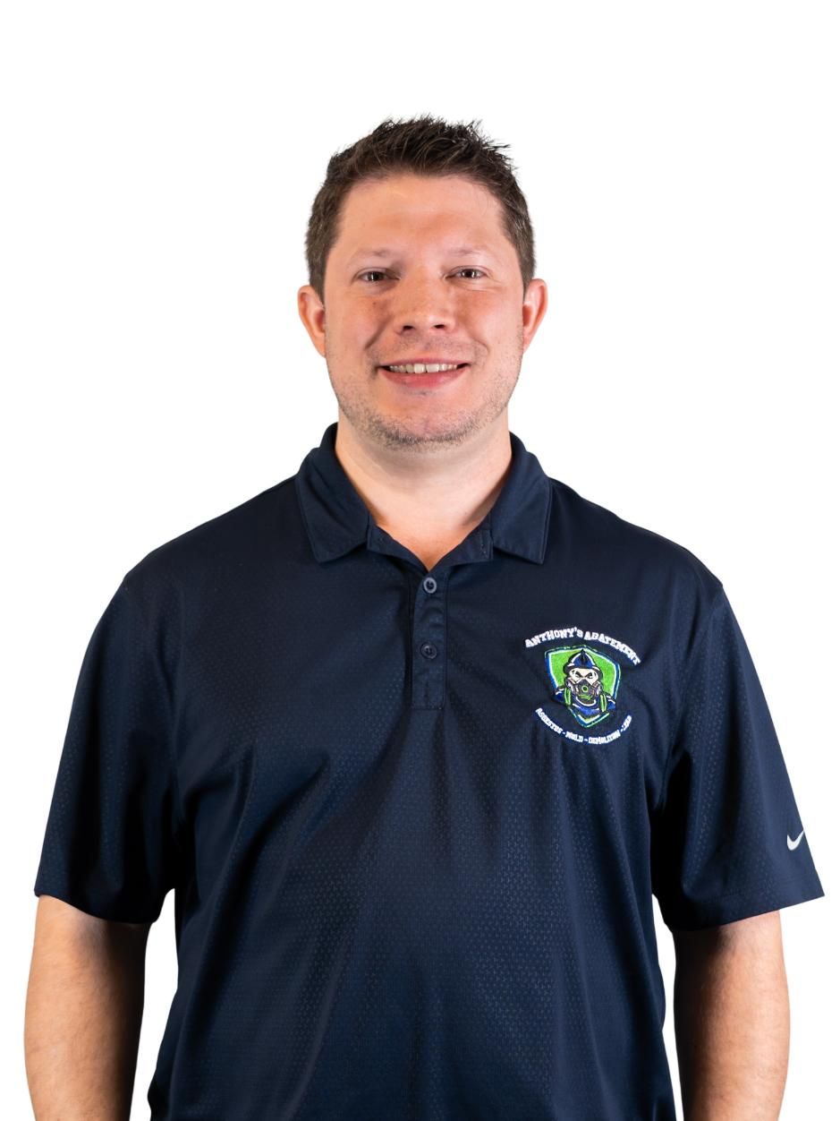 Man wearing a navy polo shirt with a logo, standing against a white background and smiling.