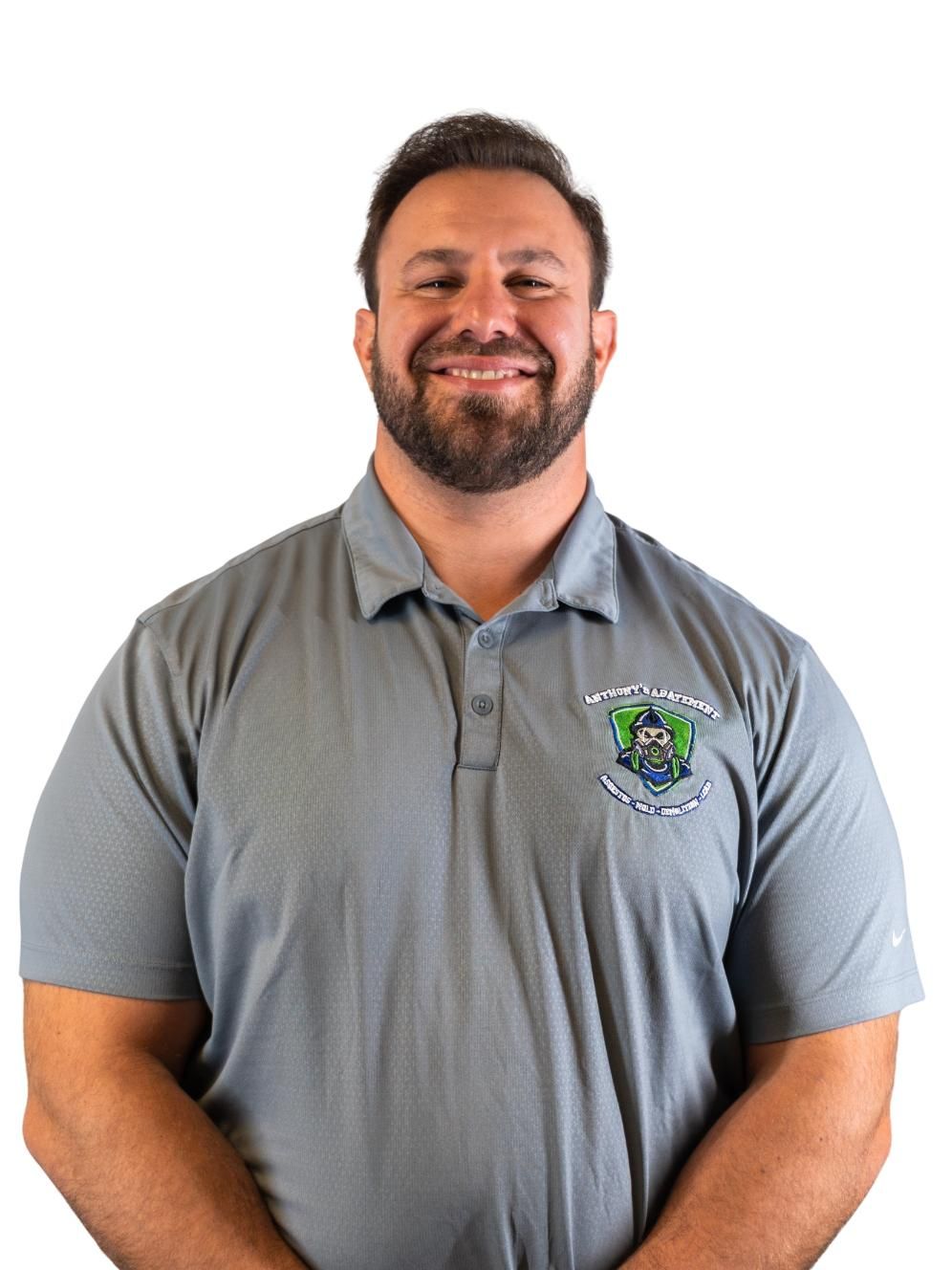 Smiling man in a gray polo shirt with a logo, standing against a white background