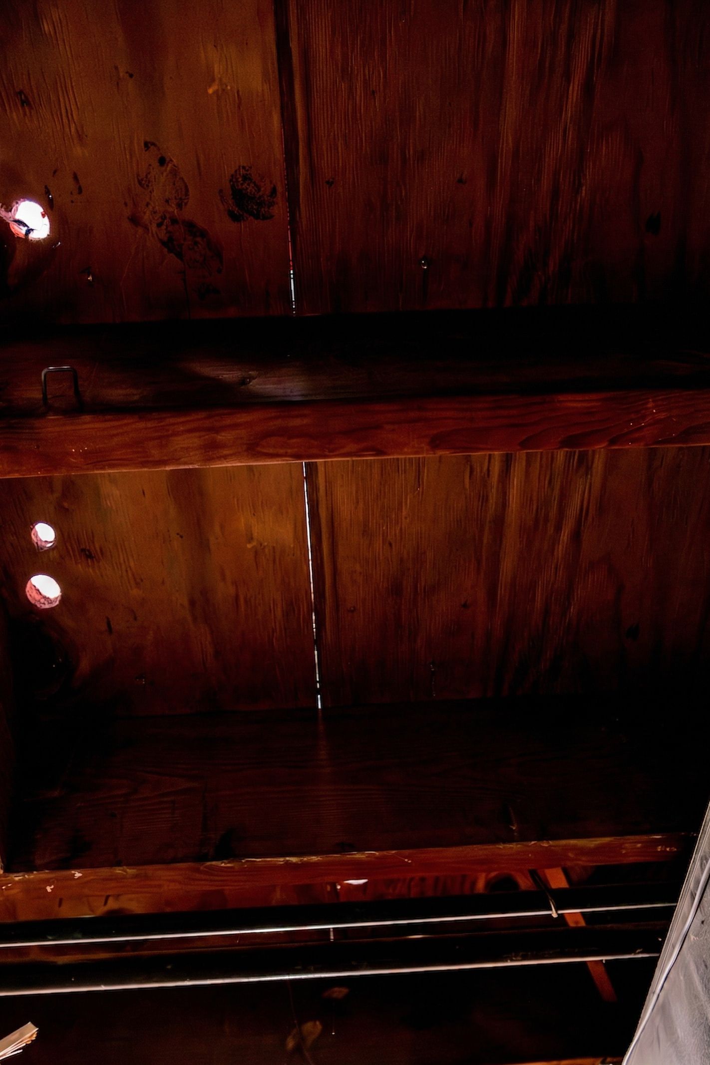 Dark wooden shelves or cabinet interior with a few white spots and a metal rack at the bottom