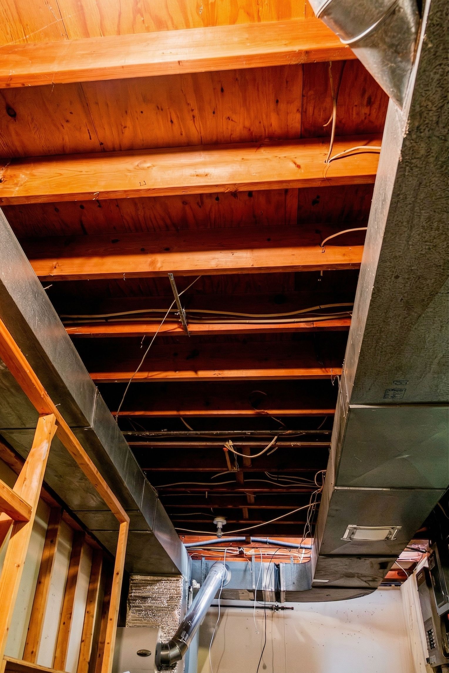 Exposed wooden ceiling beams in a construction area with hanging wires and ducts