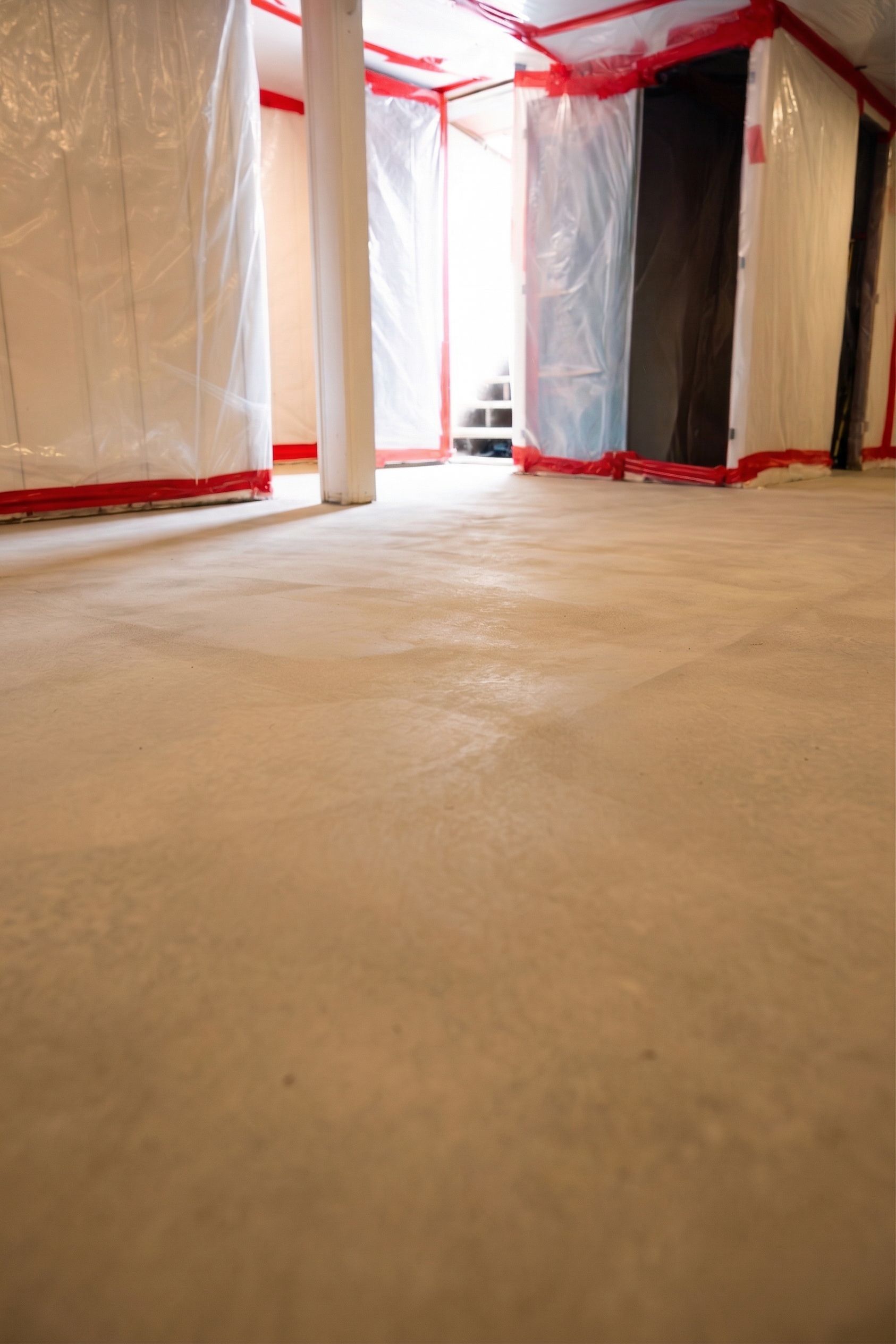 Plastic-covered room with red tape and a concrete floor, viewed from a low angle.