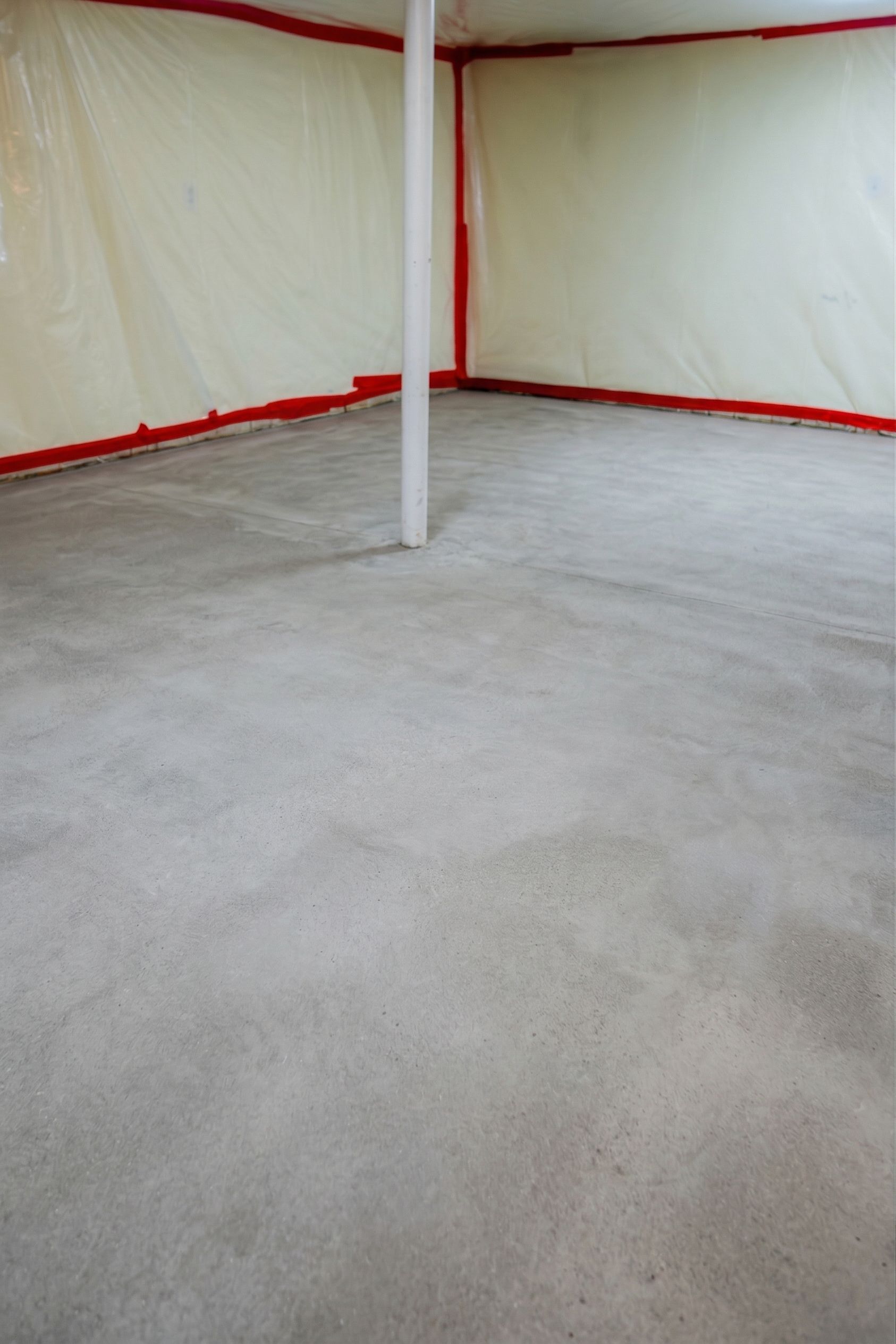 Empty room with white walls, red trim, and a concrete floor, centered on a white support pole