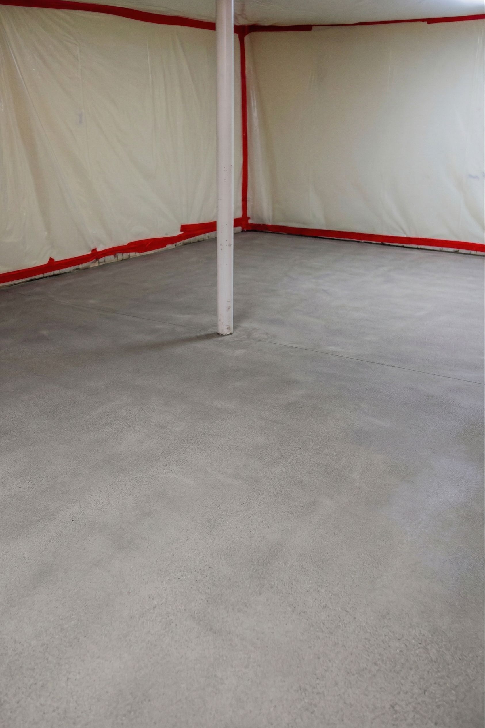 Empty room with gray concrete floor and white walls, red trim, and a central support pole.